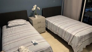 Une chambre double avec deux lits simples, une table de chevet agrémentée d’une plante et une fenêtre donnant sur un paysage agréable.