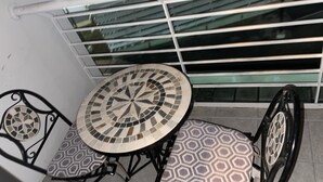 Un petit espace extérieur aménagé avec une table ronde et deux chaises, agrémenté d’un motif décoratif en mosaïque.