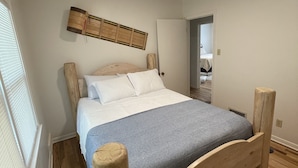Ein Bett aus Holz in einem Zimmer mit Holzboden, einer Deckenleuchte und einem Fenster mit Jalousien.