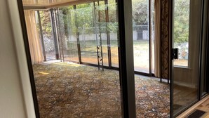 Ein Zimmer mit einer großen Schiebeglastür, die zu einem Außenbereich mit einem gemusterten Boden und einem umzäunten Garten führt.