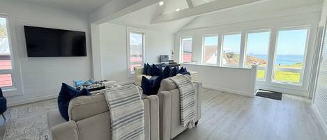 Een ruime woonkamer met een grote modulaire bank, een flatscreen televisie aan de muur en grote ramen met uitzicht op het landschap.