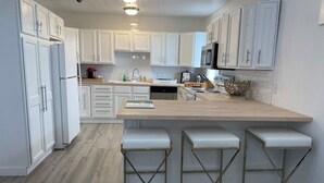 Una cocina con armarios blancos, encimera de madera y tres taburetes de bar.