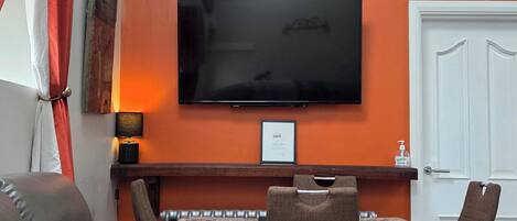 A living room with a sofa, a TV mounted on the wall, a table with chairs, and a door.