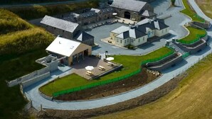 An aerial view of a large, modern building with multiple sections, including a covered outdoor area and a curved driveway. - Magical 3-Bed Stone Built Cottage - Sleeps 6 (Down)