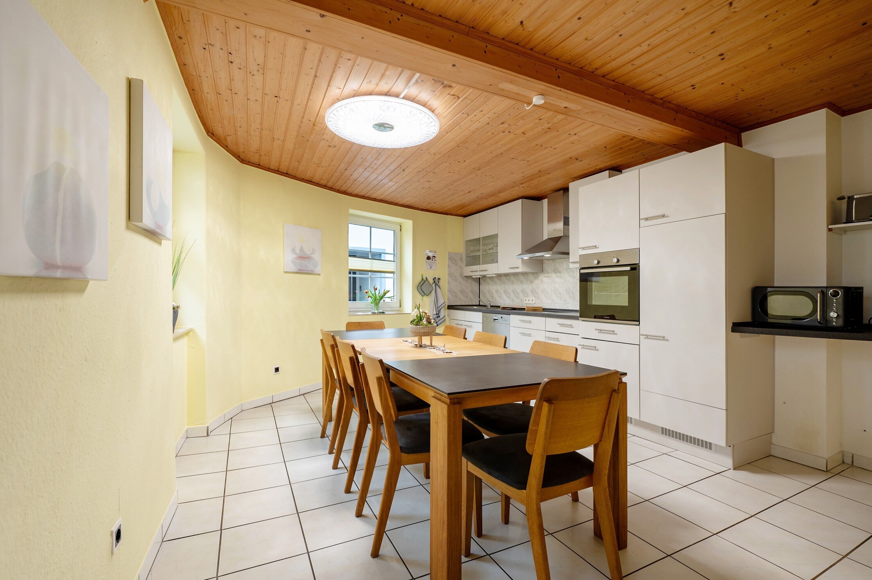 Una cocina con armarios de madera, una mesa de comedor con sillas y piso de baldosas.