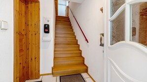 Un escalier en bois menant à l’étage supérieur, une porte avec une poignée et un thermostat fixé au mur.