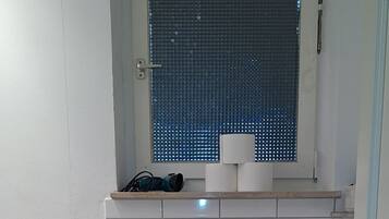 Ein Badezimmer mit Toilette, Toilettenpapier, einem Fenster mit Metallgitter und einem Handtuchhalter.