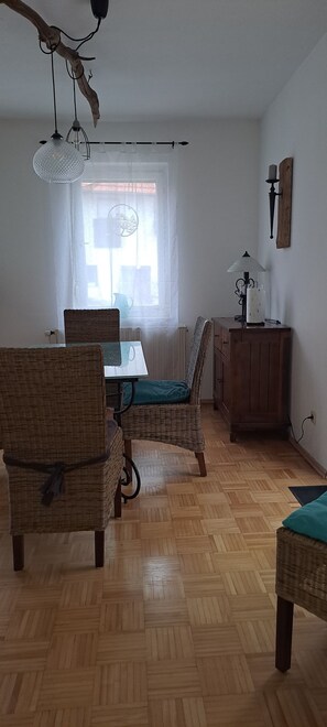 A dining area with wicker chairs, a glass table, and a wooden cabinet.