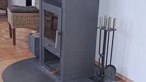 A modern fireplace with a chimney, a wooden floor, and a wicker chair in the background.