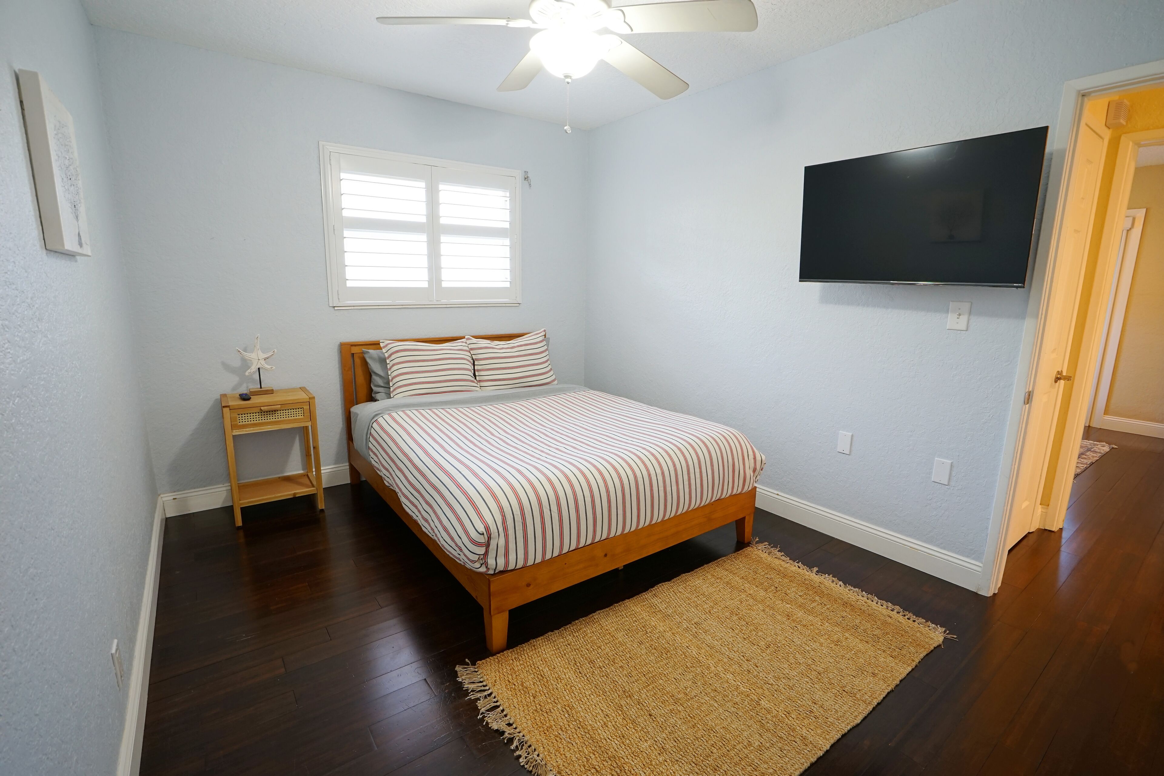 Une chambre à coucher avec un lit, une table de chevet, un ventilateur de plafond, une télévision et une fenêtre.