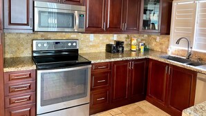 Una cocina con gabinetes de madera oscura, electrodomésticos de acero inoxidable, encimera de granito y pileta integrada.