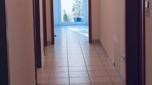 Un couloir avec un sol carrelé, une porte sur la droite et une fenêtre au fond.