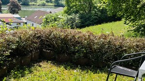 Un espace extérieur aménagé avec des sièges blancs, offrant une vue sur une rivière et des collines boisées.