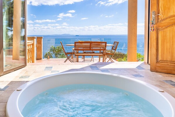 Un jacuzzi avec vue sur la mer, une table et des chaises en bois, et une porte vitrée.