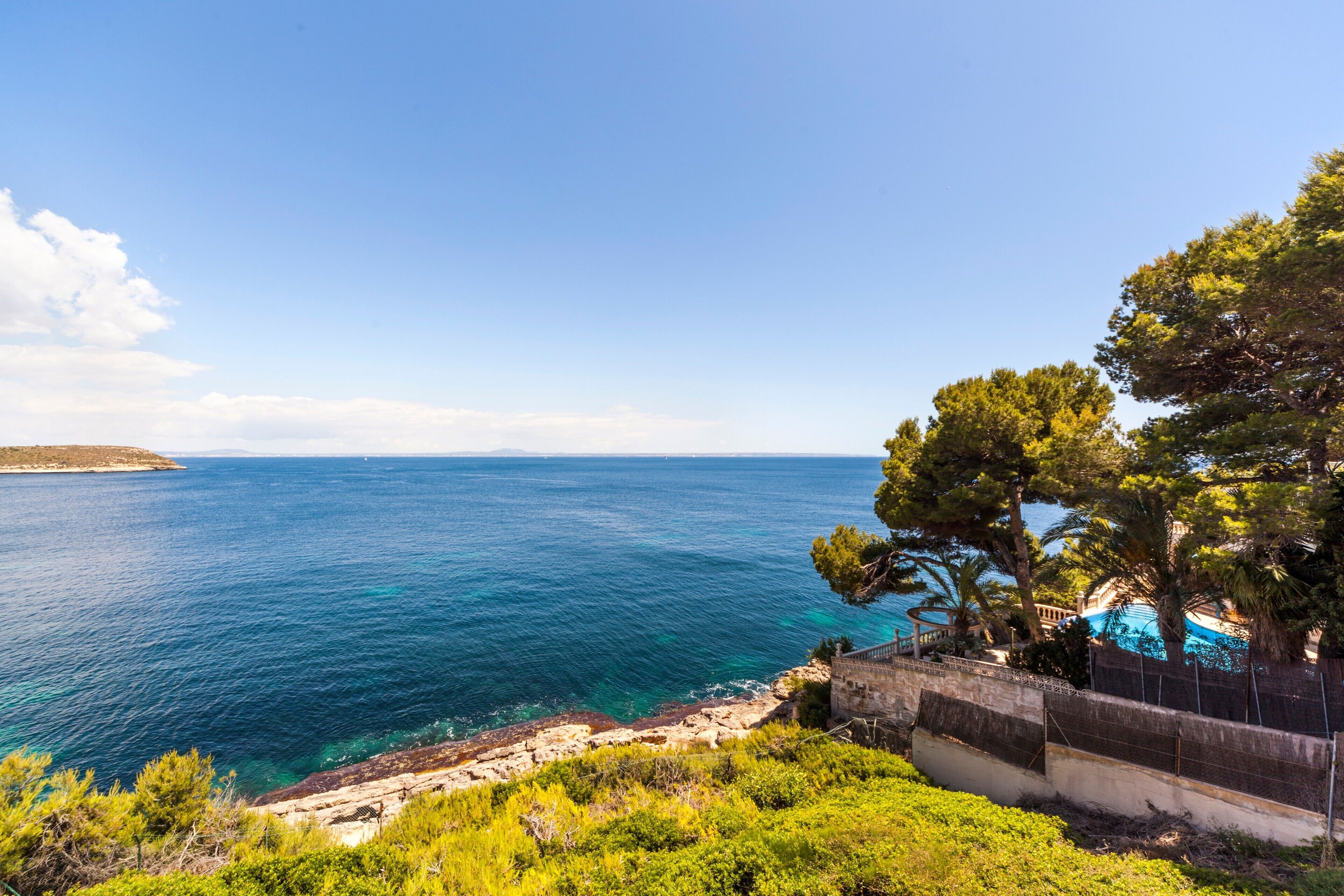 A coastal view with a clear sky, a rocky shoreline, and a building with a pool.