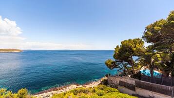 A coastal view with a clear sky, a rocky shoreline, and a building with a pool.