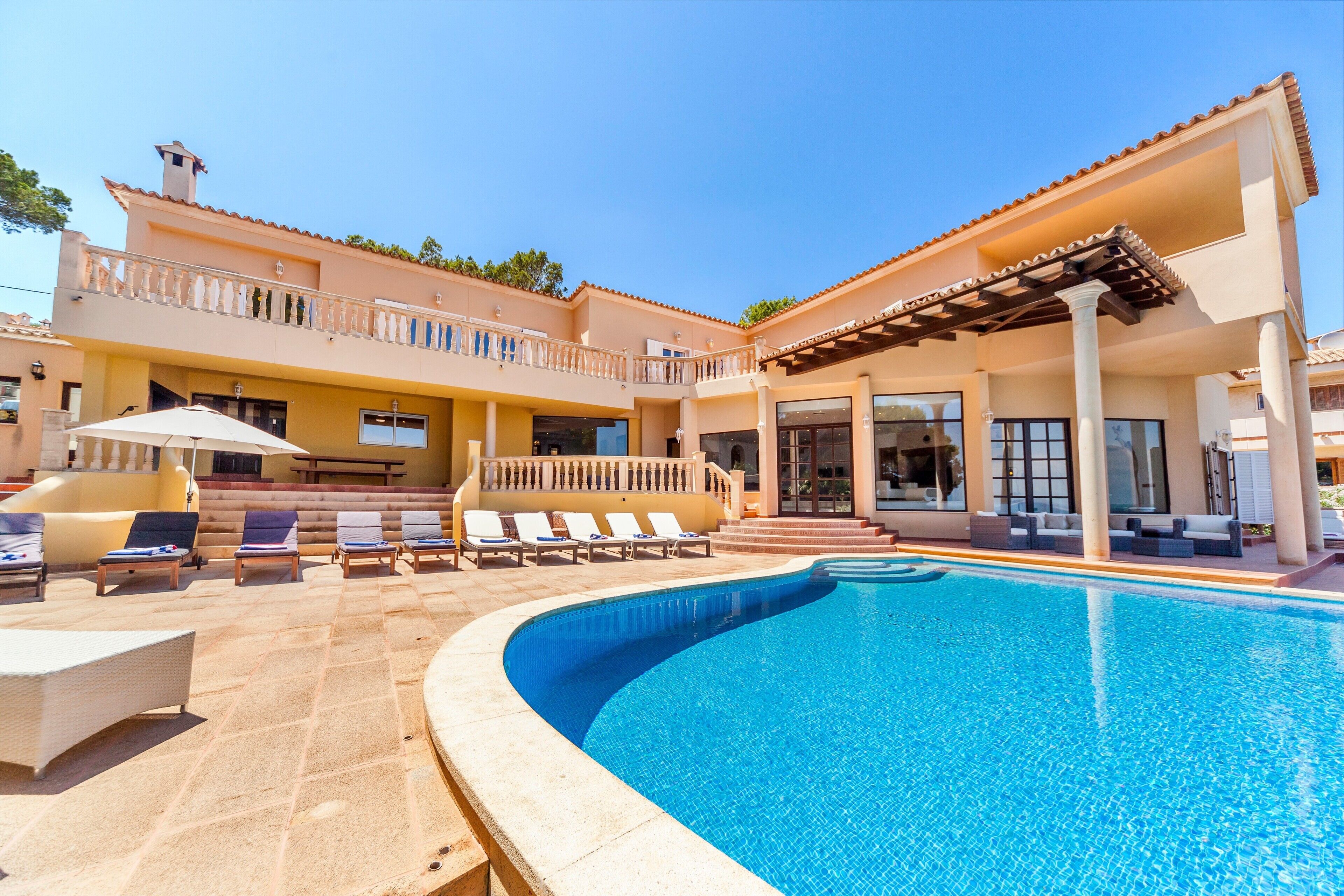 Un espace aménagé au bord de la piscine, avec des chaises longues, une pergola et un bâtiment doté de balcons.