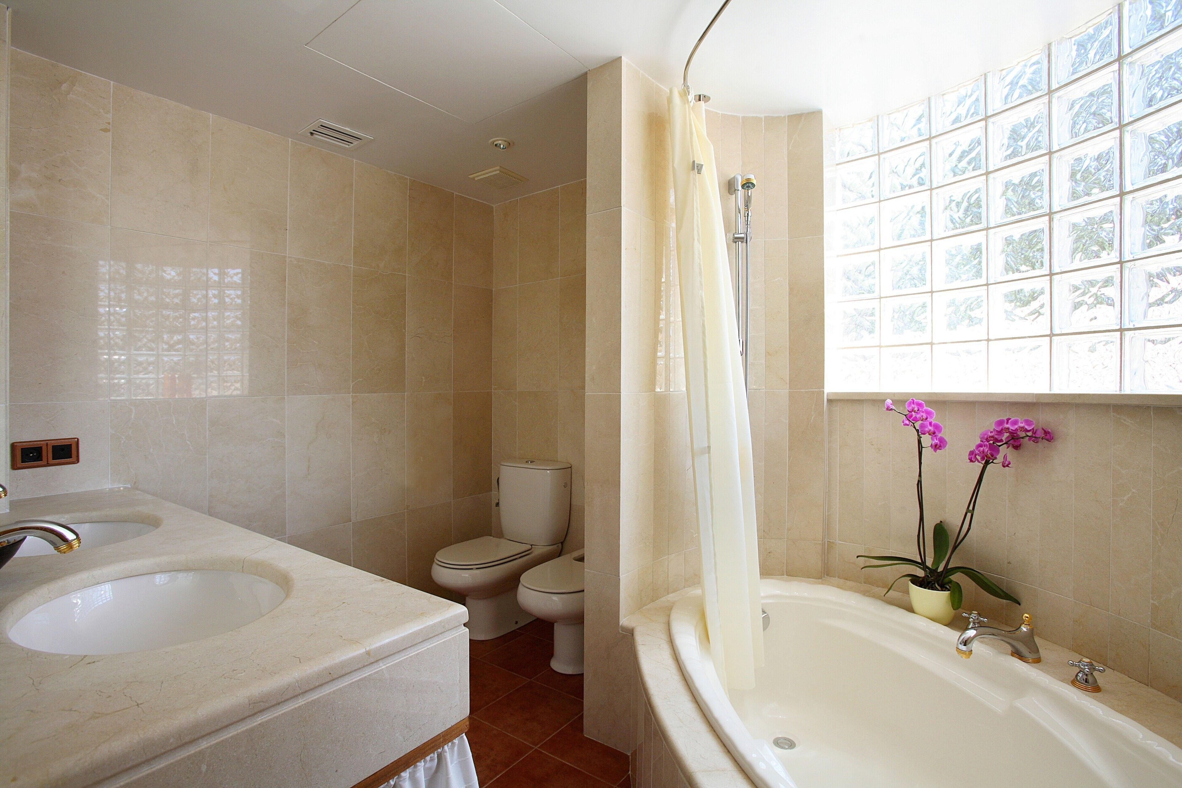 A bathroom with a bathtub, two sinks, a toilet, and a window with a view.