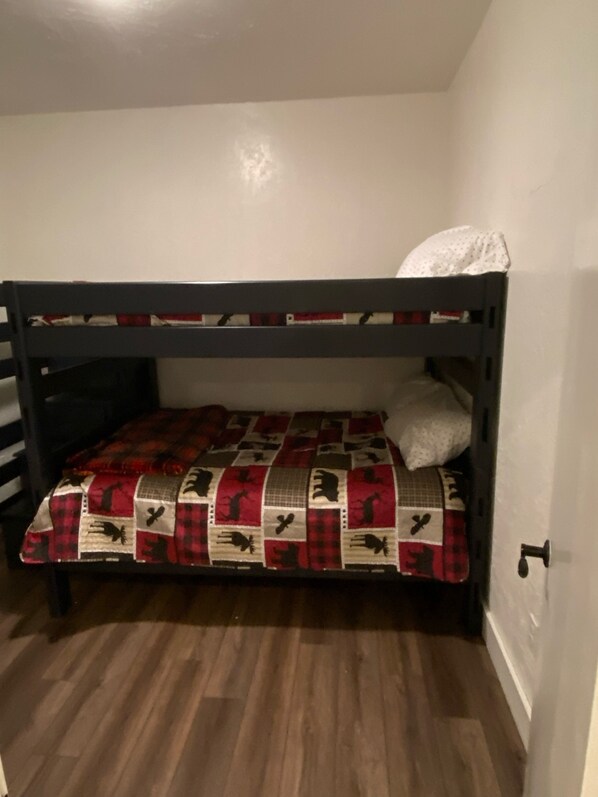 A bunk bed with a red and black quilt, a white pillow, and a wooden floor.