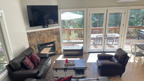 A living room with a stone fireplace, a flat-screen TV, a large window, and a patio area with outdoor furniture.