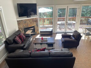 A living room with a stone fireplace, a flat-screen TV, a large window, and a patio area with outdoor furniture.