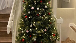 A Christmas tree decorated with ornaments and lights, placed in a stairwell with white railings and wooden steps.