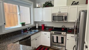 A modern kitchen with white cabinets, stainless steel appliances, a granite countertop, and a window with a view of the outside.