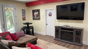 A living room with a sectional sofa, a flat-screen TV, a fireplace, and a door with a poster.