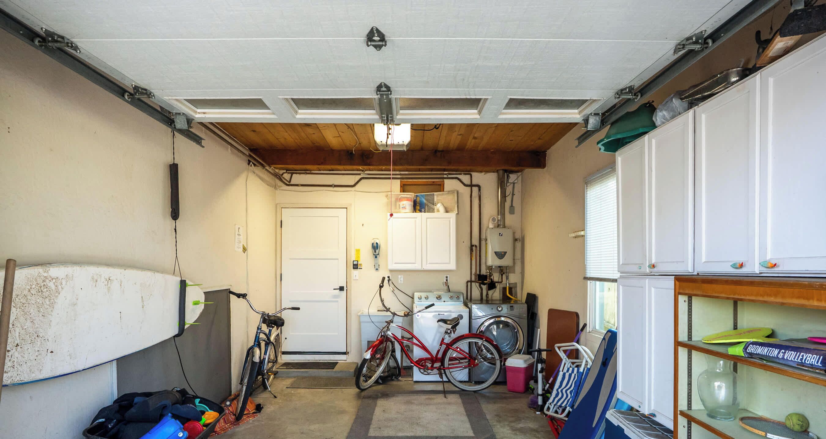 A garage with a bicycle, a surfboard, and a shelf with sports equipment.