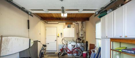 A garage with a bicycle, a surfboard, and a shelf with sports equipment.