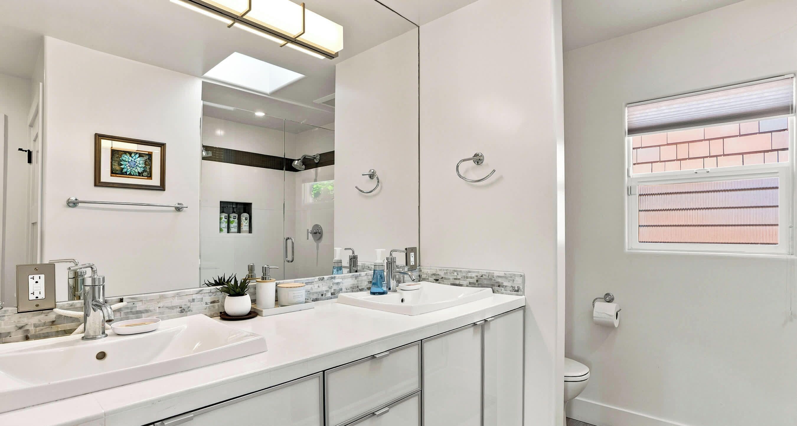 Un baño moderno con dos lavamanos, un espejo grande y un inodoro.
