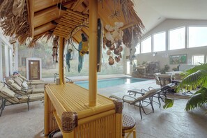 Un espace aménagé au bord de la piscine, avec des chaises longues, une table en bambou et un toit de chaume.