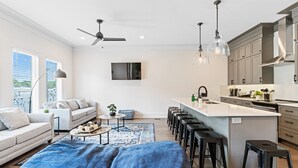 Eine moderne Küche mit Kochinsel, Barhocker und Essbereich inklusive Sofa und Couchtisch.