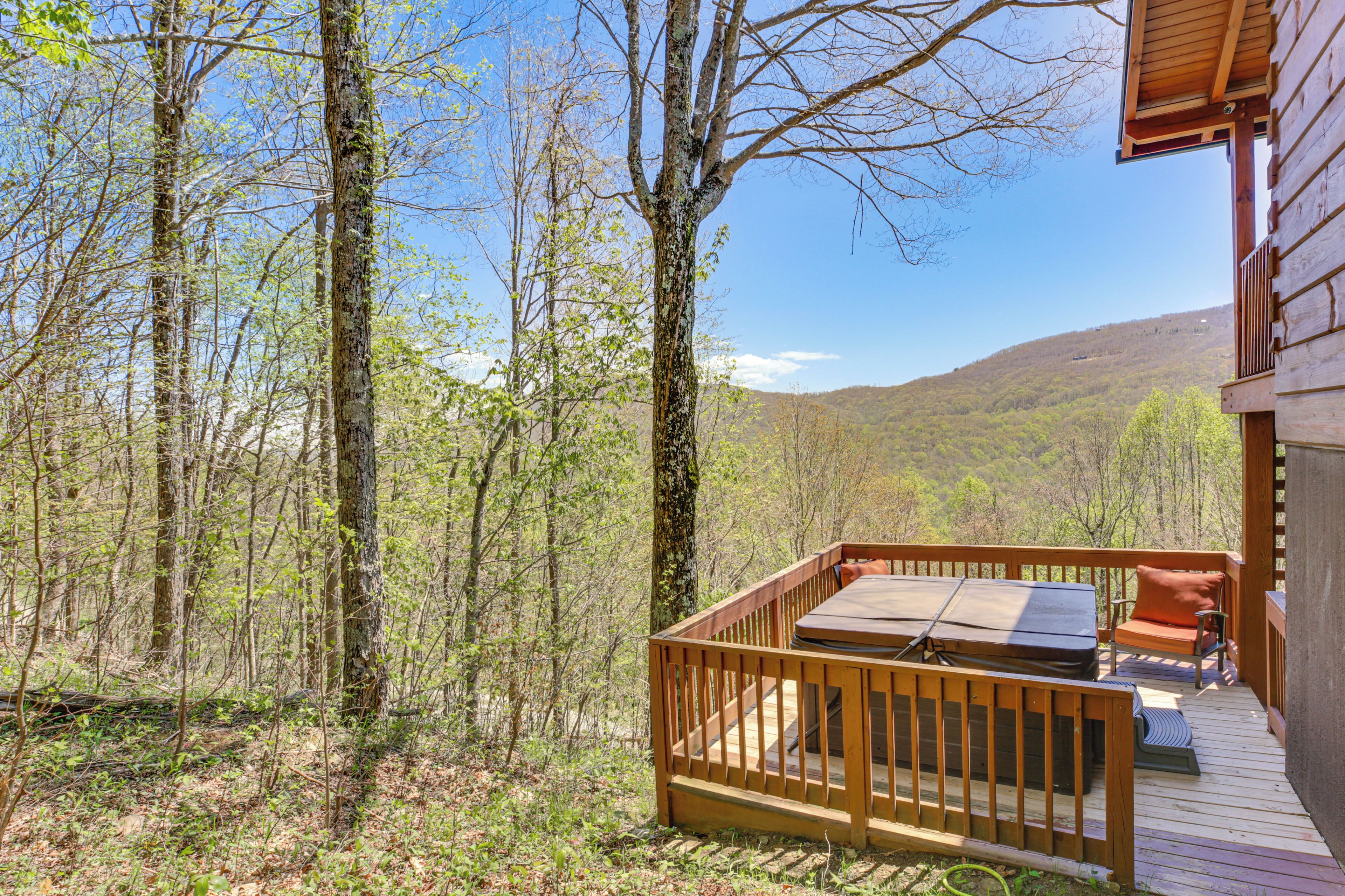 A wooden deck with a table and chairs, surrounded by trees and a mountain view.