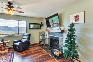Un salon avec une cheminée, un téléviseur fixé au mur, un fauteuil inclinable et un sapin de Noël.