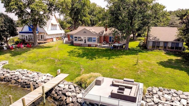 A house with a deck overlooking a body of water, surrounded by a grassy yard and trees.