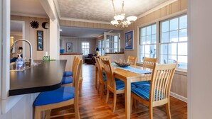 A dining area with a wooden table and chairs, a chandelier, and large windows.