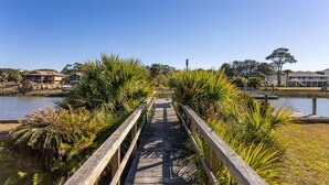 A wooden boardwalk leading to a waterfront area with houses in the background.