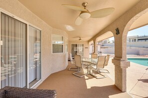 Un'area patio coperta con tavolo e sedie, una ventola a soffitto e vista su una piscina.