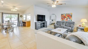 A spacious living room with a grey sofa, a coffee table, and a TV. There is a dining area with chairs and a table, and a kitchen area with a counter and cabinets. - Lake Havasu Home - 2 Mi from Main Launch Ramp! (Lake Havasu City)