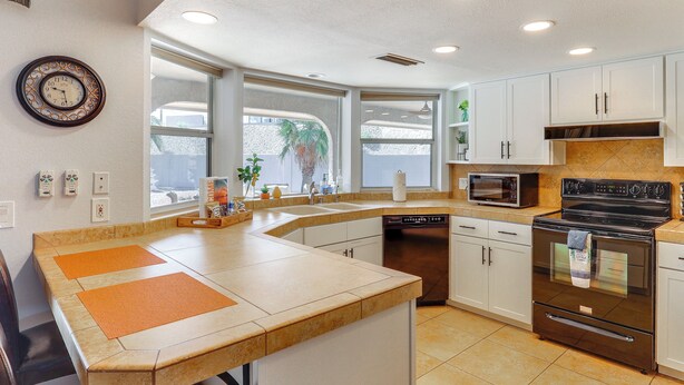 A modern kitchen with a curved island, built-in microwave, stainless steel appliances, and large windows offering views of the outdoors. - Lake Havasu Home - 2 Mi from Main Launch Ramp! (Lake Havasu City)