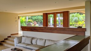 Ein modernes Interieur mit einer Treppe zu einem Balkon, einer Couch und Blick auf üppiges Grün draußen.