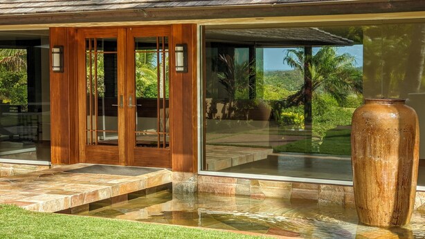 Ein modernes Haus mit einer großen Glasdoor, einem Steinweg, der zum Eingang führt, und einem großen Strauß auf der Terrasse.