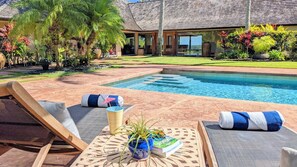 A poolside area with lounge chairs, towels, and a small table with a plant and books. - Private Villa on 3 acres with Pool and Spa TVNC-4195 (Kilauea)