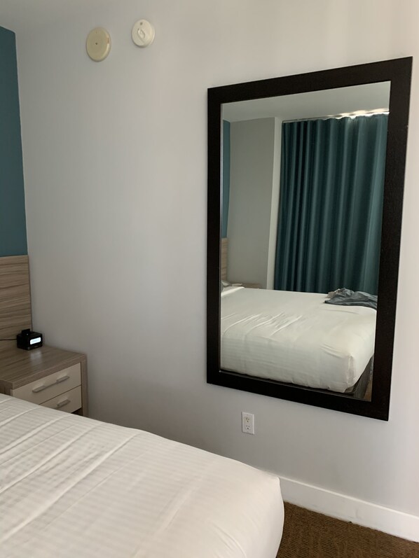 A hotel room with a bed, a nightstand, a wall-mounted mirror, and a wall socket.