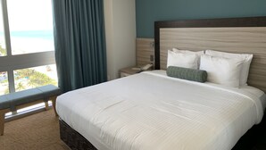 Une chambre d’hôtel avec un grand lit, une vue sur la plage et une fenêtre avec des rideaux.