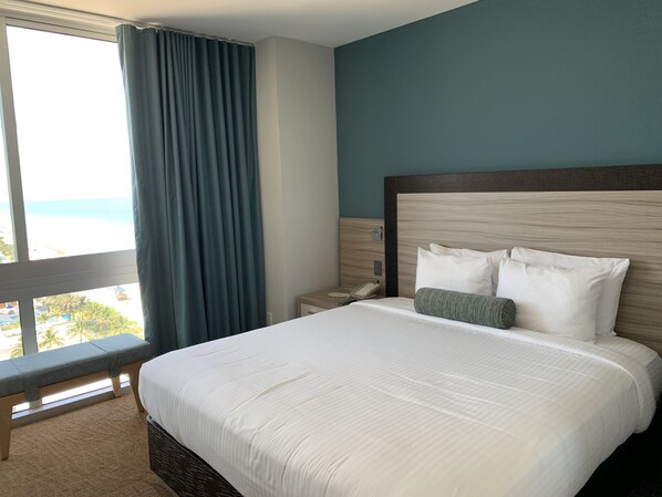 A hotel room with a large bed, a view of the beach, and a window with curtains.