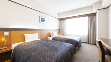 A hotel room with two beds, a desk, and a large window with curtains.