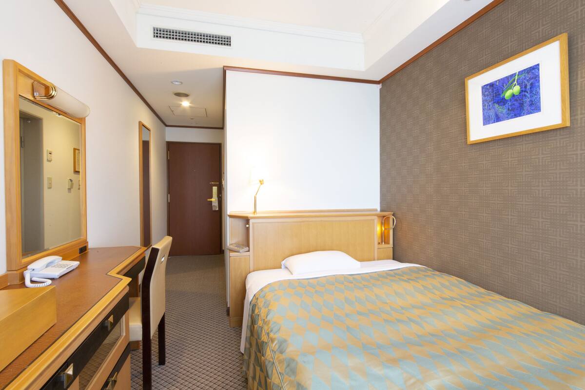 A hotel room with a bed, a desk with a telephone, a mirror, and a picture on the wall.