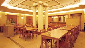 A spacious dining area with multiple wooden tables and chairs, a central column, and a long counter with a mirror. - Hotel Le Port Kojimachi (Tokyo)